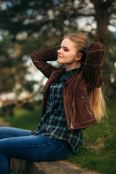 Una hermosa chica está caminando por el terraplén. Cabello rubio y chaqueta marrón. Primavera . —  Fotos de Stock