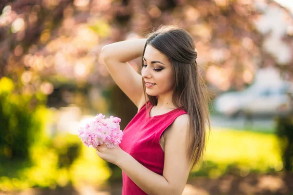 Bella ragazza in posa per il fotografo sullo sfondo di alberi rosa in fiore. Primavera. Sakura . — Foto Stock