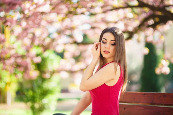 Jong meisje poseren voor een foto. Roze bloeiende bomen op de achtergrond. Lente. Sakura. — Stockfoto