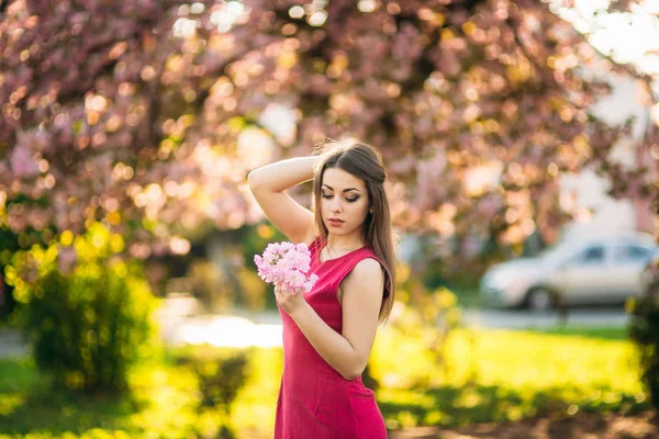 Jong meisje poseren voor een foto. Roze bloeiende bomen op de achtergrond. Lente. Sakura. — Stockfoto