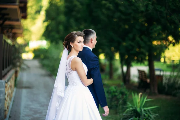 Schönes Paar, das am Hochzeitstag im Park spazieren geht. sonniges Wetter. — Stockfoto