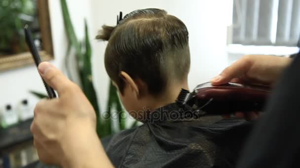 Мальчик стрижется парикмахером, сидя в кресле в парикмахерской . — стоковое видео