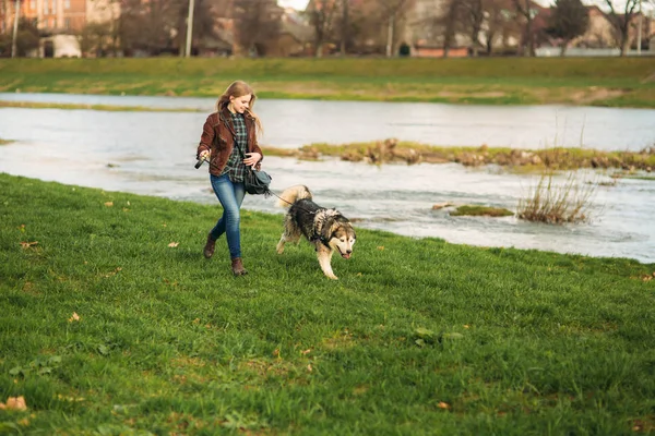 Ein schönes Mädchen läuft die Böschung entlang. blonde Haare und braune Jacke. Frühling. — Stockfoto