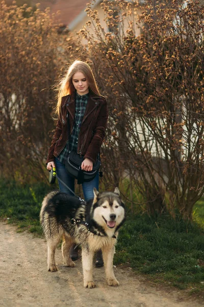 Une belle fille marche le long du remblai. Cheveux blonds et veste brune. Printemps . — Photo