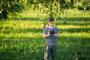 Çizgili bir gömlek küçük çocuk dürbün ile görünüyor. Bahar, güneşli havalarda.