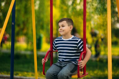 Salıncakta sallanmak, çizgili tişört içinde küçük bir çocuk oyun oynuyor. Bahar, güneşli havalarda.