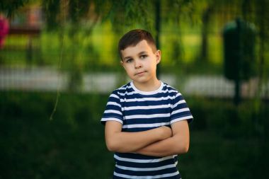 Çizgili bir gömlek içinde küçük bir çocuk gülümseyen ve tezahürat. Bahar, güneşli havalarda.