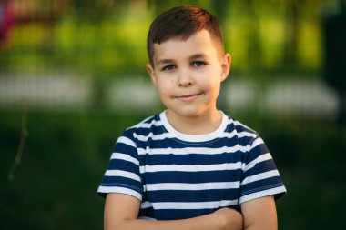 Çizgili bir gömlek içinde küçük bir çocuk gülümseyen ve tezahürat. Bahar, güneşli havalarda.