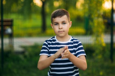 Çizgili bir gömlek içinde küçük bir çocuk gülümseyen ve tezahürat. Bahar, güneşli havalarda.