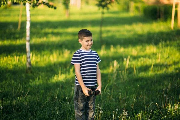 Liten pojke i en randig t-shirt ser genom kikare. Våren, soligt väder. — Stockfoto