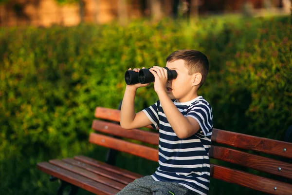 Little boy in a striped t-shirt looks through binoculars .Spring, sunny weather. — Stock Photo, Image