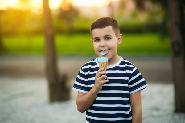 Egy kis fiú a csíkos póló kék fagylalt eszik. Tavasz, napsütés. — Stock Fotó