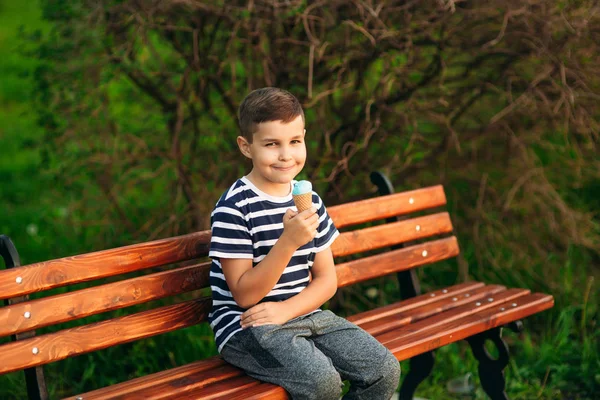 Ein kleiner Junge im gestreiften T-Shirt isst blaues Eis. Frühling, sonniges Wetter. — Stockfoto