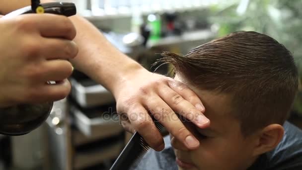 Маленький хлопчик отримує зачіску за перукарнею сидячи в кріслі в перукарні . — стокове відео
