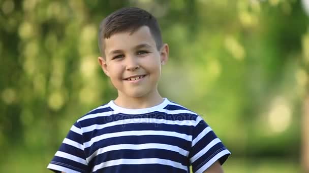 Um menino em uma camiseta listrada está sorrindo e alegria.Primavera, tempo ensolarado . — Vídeo de Stock