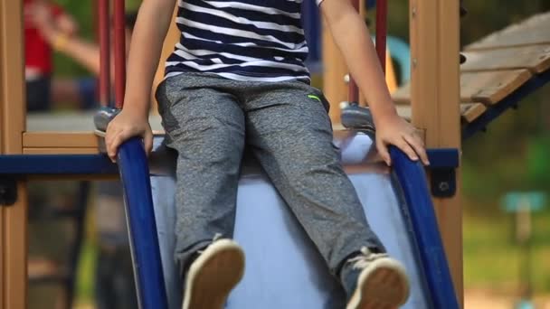 Маленький хлопчик у смугастій футболці грає на ігровому майданчику, гойдається на гойдалці. Весна, сонячна погода . — стокове відео