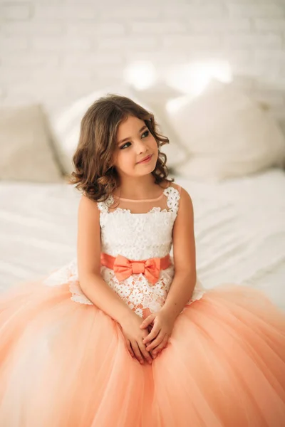 Όμορφο κοριτσάκι με καστανά μαλλιά σε ένα φόρεμα ροδακινί. Πόζες για έναν φωτογράφο — Φωτογραφία Αρχείου