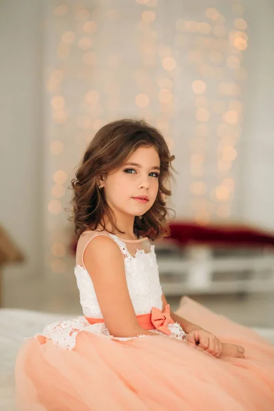 Маленькая красивая девочка с каштановыми волосами в персиковом платье. Позы для фотографа — стоковое фото