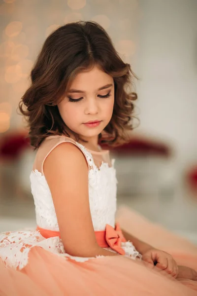 Petite belle fille aux cheveux bruns dans une robe de couleur pêche. Poses pour un photographe — Photo