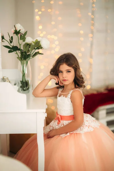 Kleines schönes Mädchen mit braunen Haaren in einem pfirsichfarbenen Kleid. posiert für einen Fotografen — Stockfoto