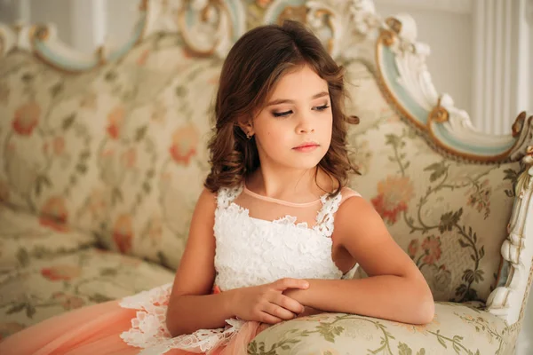 Little beautiful girl with brown hair in a Peach-colored dress. Poses for a photographer
