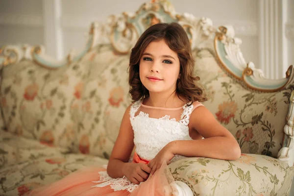 Маленькая красивая девочка с каштановыми волосами в персиковом платье. Позы для фотографа — стоковое фото