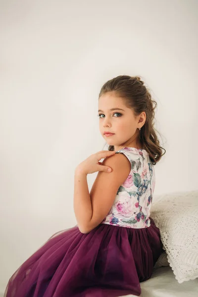 Mooi meisje in een paarse jurk en bloem blouse poseren voor een fotograaf. — Stockfoto