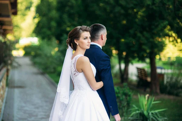 Schönes Paar, das am Hochzeitstag im Park spazieren geht. sonniges Wetter. — Stockfoto