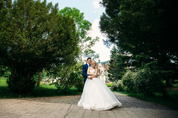 De pasgetrouwden lopen in het park op de huwelijksdag. De bruid en bruidegom genieten op de huwelijksdag. Zonnig weer. Lente. — Stockfoto