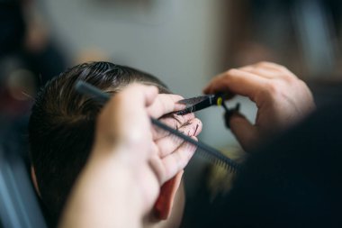 Çocuğun saçlarını Kuaför içinde bir sandalyede oturur.