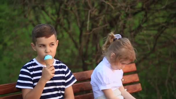 Boy and girl are sitting on the bench. Run around the park and blow dandelions — Stock Video