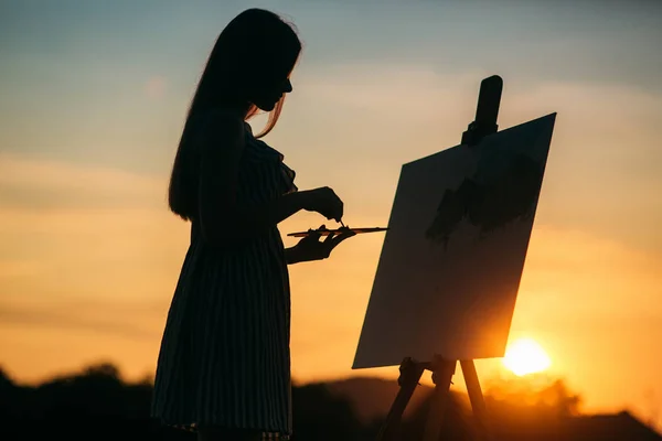 Silhouet van een meisje. Het blonde meisje schildert een schilderij op het canvas met de hulp van verven. — Stockfoto