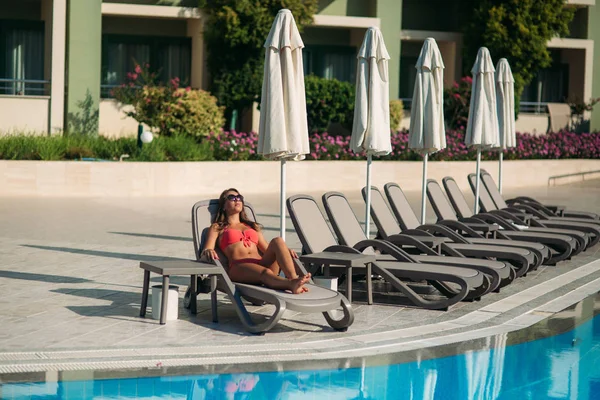 Menina sexy em uma roupa de banho rosa banhos de sol na piscina . — Fotografia de Stock