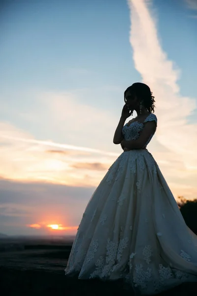 Jovem no vestido de noiva no fundo da cidade ao pôr do sol . — Fotografia de Stock