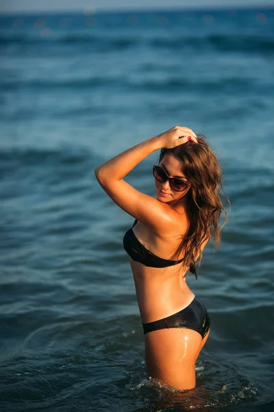 Sexy chica tomando el sol en una playa de arena y se sienta en la orilla del mar — Foto de Stock