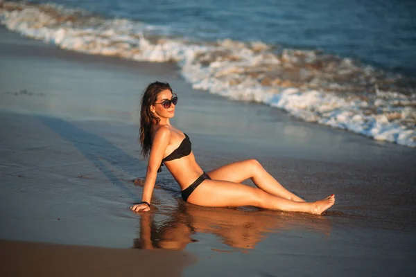 Сексуальная девушка загорает на песчаном пляже и сидит на берегу моря — стоковое фото