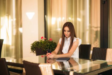 İş kadını çalışmak için bir tablet ve telefon kullanır. Kafede kız gülümsüyor