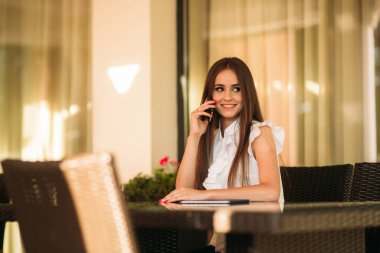 İş kadını çalışmak için bir tablet ve telefon kullanır. Kafede kız gülümsüyor