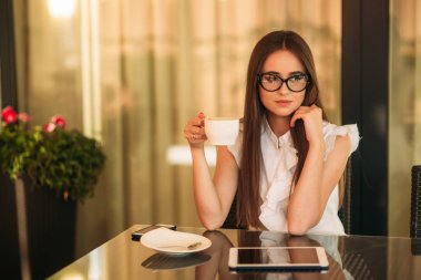 İş kadını çalışmak için bir tablet ve telefon kullanır. Kafede kız gülümsüyor