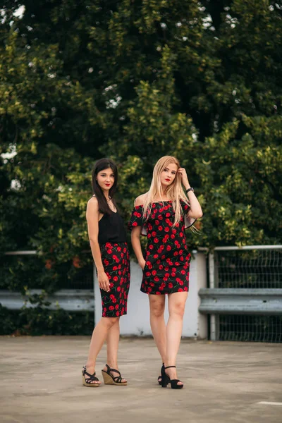 Hermosas chicas posando para el fotógrafo. Dos hermanas vestidas de negro y rojo. Sonrisa, día soleado, verano . — Foto de Stock