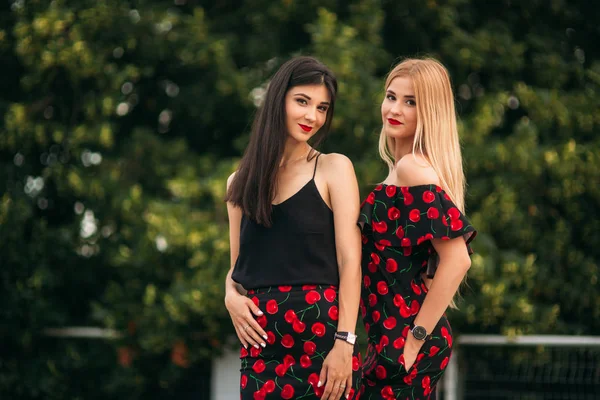 Schöne Mädchen, die für den Fotografen posieren. zwei Schwestern in schwarz-rotem Kleid. Lächeln, sonniger Tag, Sommer. — Stockfoto