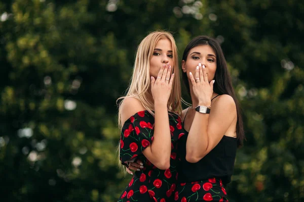 Smukke piger poserer for fotografen. To søstre i sort og rød kjole. Smil, solskinsdag, sommer . - Stock-foto