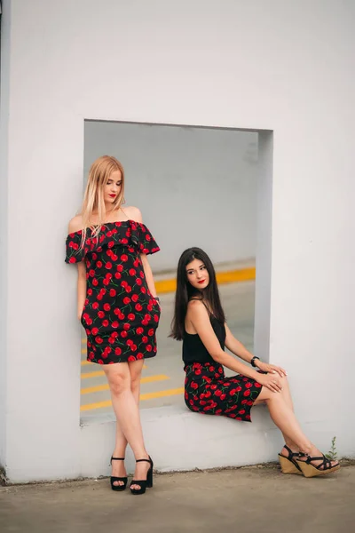 Schöne Mädchen, die für den Fotografen posieren. zwei Schwestern in schwarz-rotem Kleid. Lächeln, sonniger Tag, Sommer. — Stockfoto