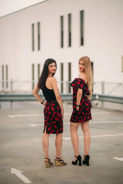 Hermosas chicas posando para el fotógrafo. Dos hermanas vestidas de negro y rojo. Sonrisa, día soleado, verano . — Foto de Stock