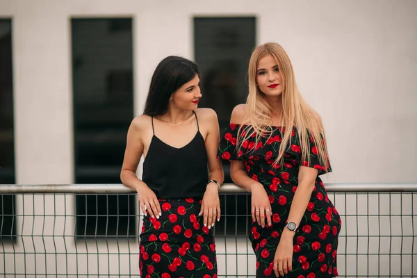 Schöne Mädchen, die für den Fotografen posieren. zwei Schwestern in schwarz-rotem Kleid. Lächeln, sonniger Tag, Sommer. — Stockfoto