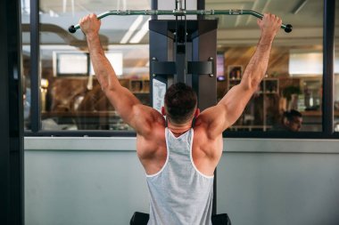 Genç bir atlet spor salonunda eğitiyor. Sırt ve göğüs kaslarının gösterir