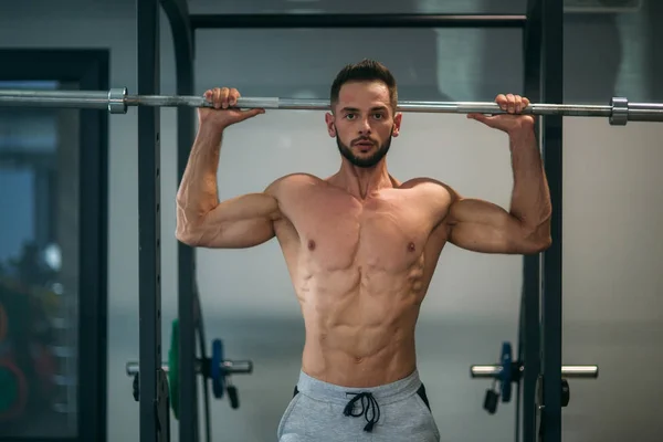 Um jovem atleta treina no ginásio. Mostra os músculos das costas e do peito — Fotografia de Stock