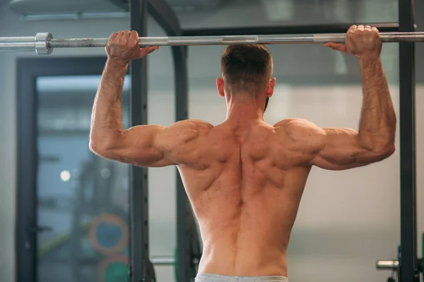 Un joven atleta entrena en el gimnasio. Muestra los músculos de la espalda y el pecho — Foto de Stock