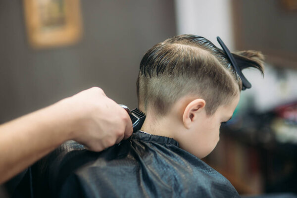 Little Boy Getting Haircut By Barber While Sitting In Chair At Barbershop.