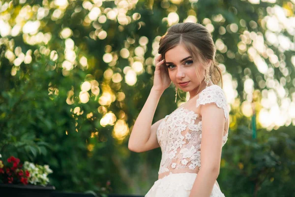 Junges Mädchen im Hochzeitskleid im Park posiert für Fotografen. Sonnenwetter, Sommer. — Stockfoto